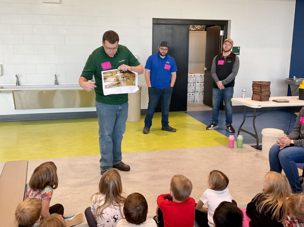 Domtar employees guide Riverside Elementary first graders through the steps of papermaking, showing students how pulp is formed before it becomes a finished sheet.