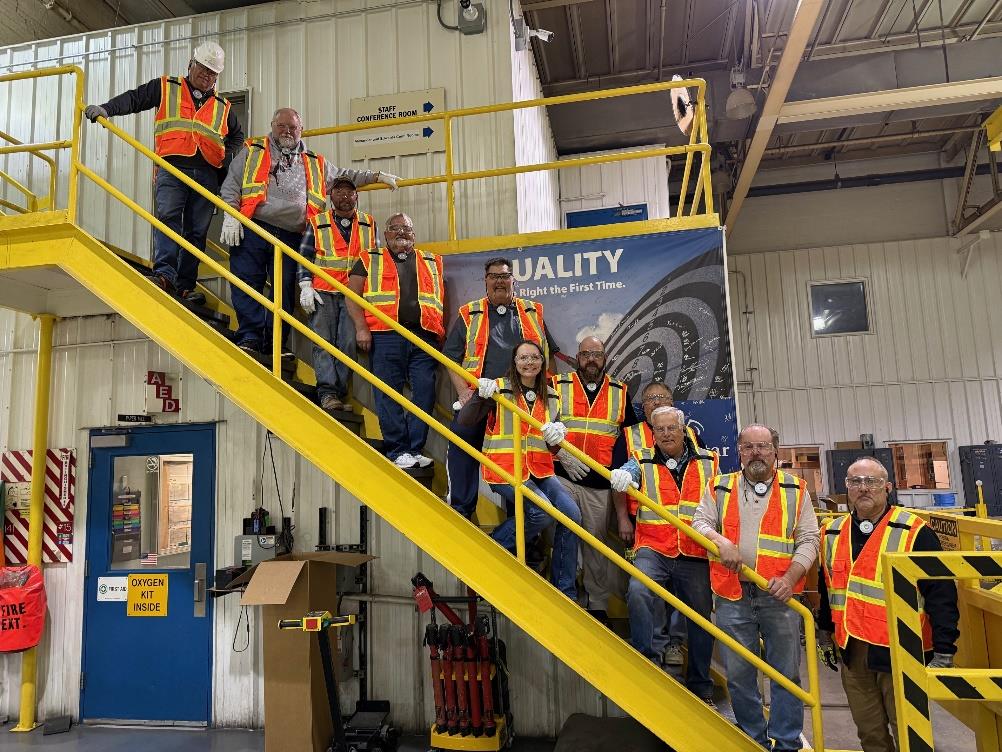 Group of Nekoosa Mill staff and city officials wearing safety vests and hard hats standing on an industrial staircase during a facility tour.
